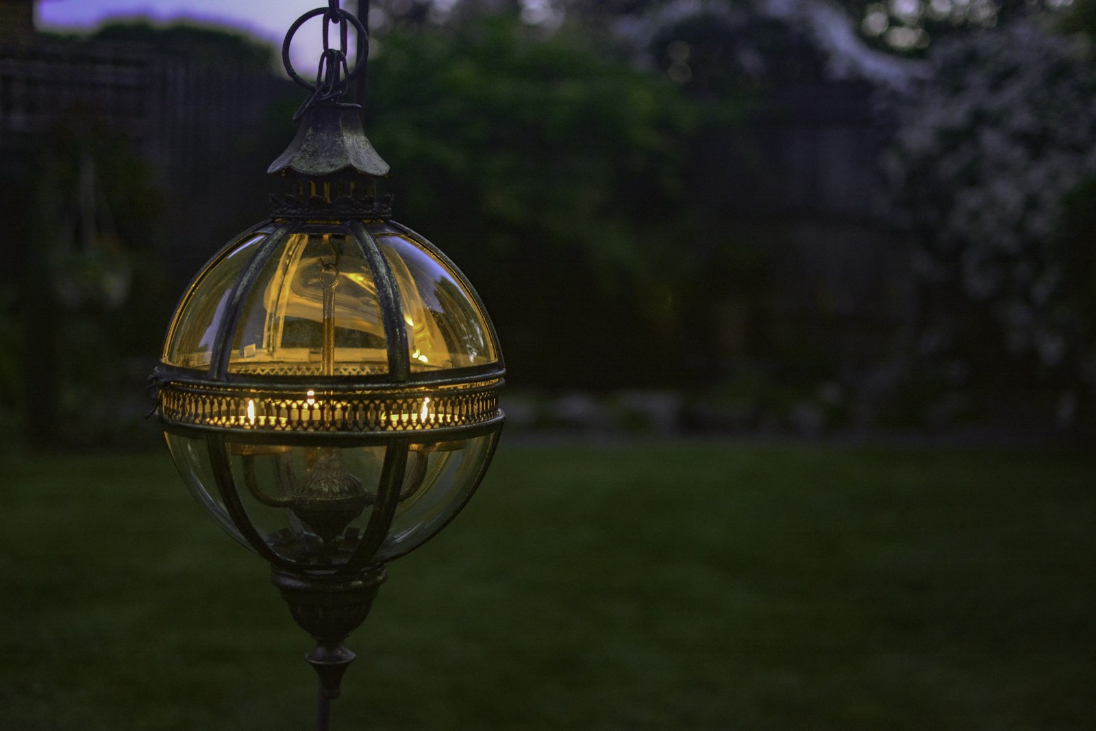 Ampoule à lumière chaude allumée devant un jardin sombre en soirée.