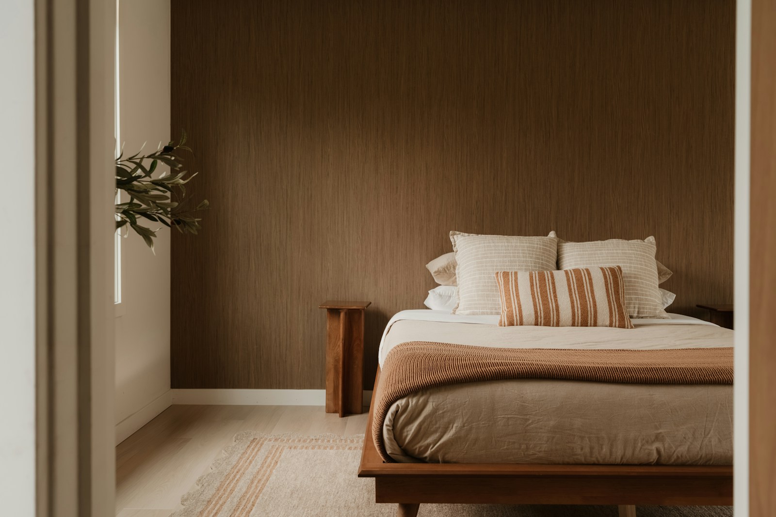 Chambre aux murs terracotta mat avec lit en bois et linge de lit en lin