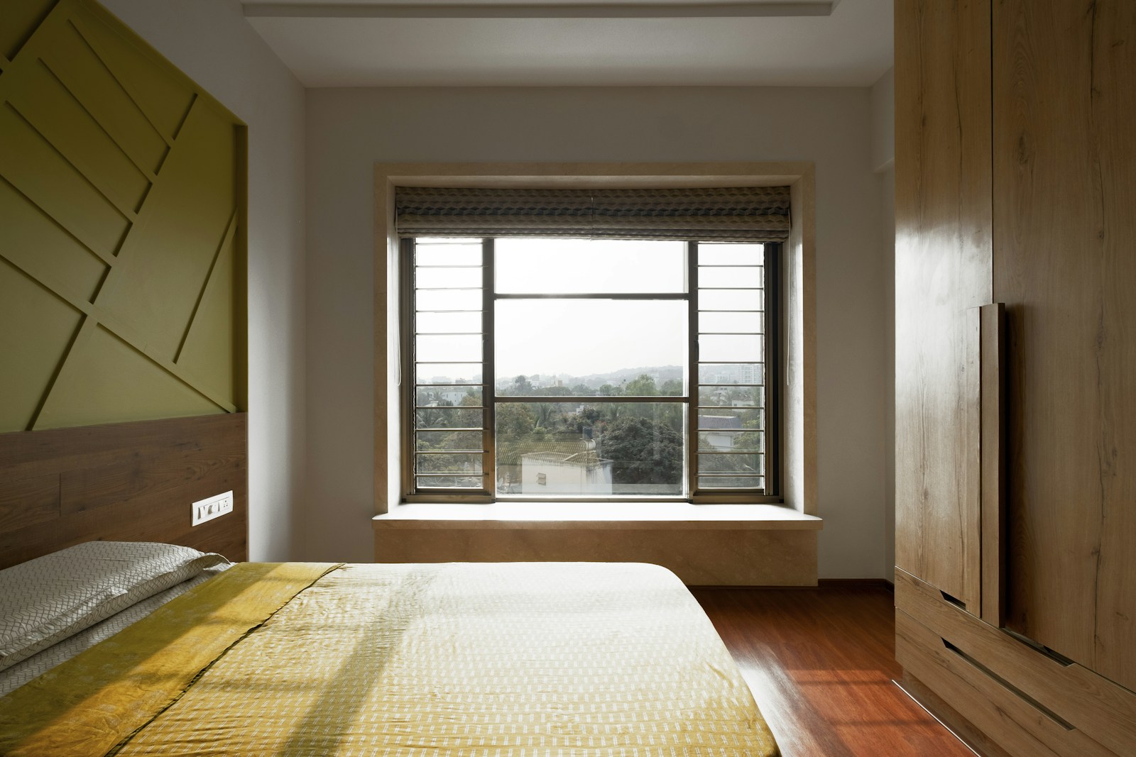 Chambre dont la fenêtre fait face au lit, mobilier en bois et lumière naturelle.