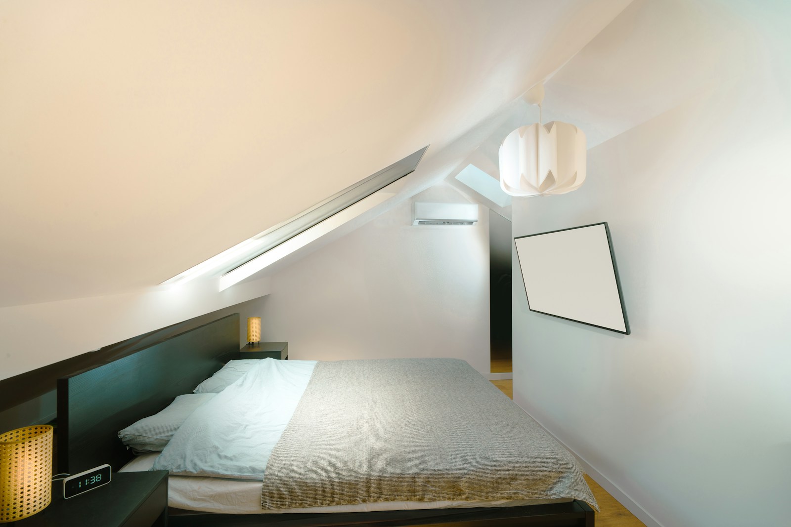 Chambre vide sous les combles, plafond rampant et parquet en bois clair.
