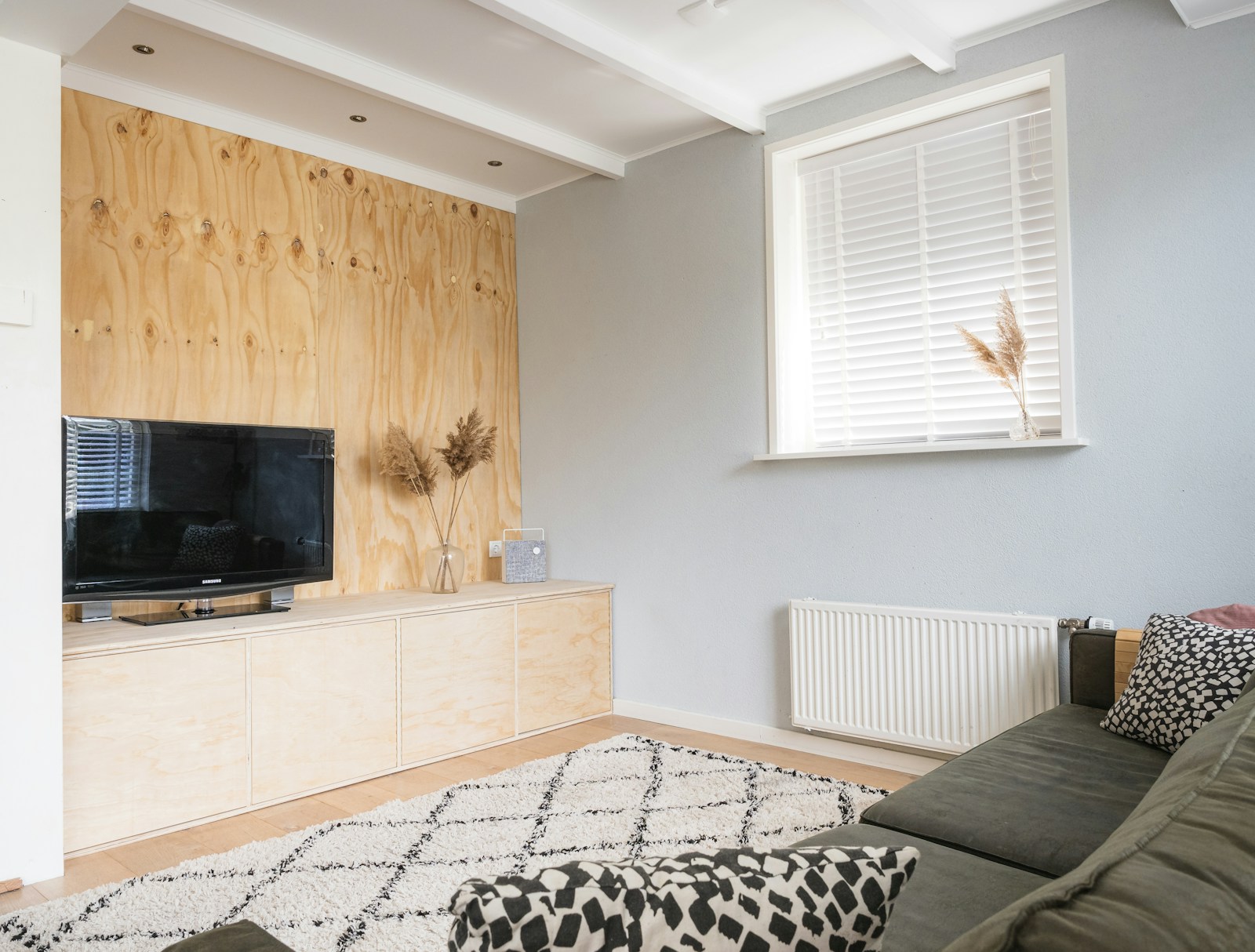 Coin de salon avec un écran posé sur un meuble bas en bois, éclairé par la lumière du jour.