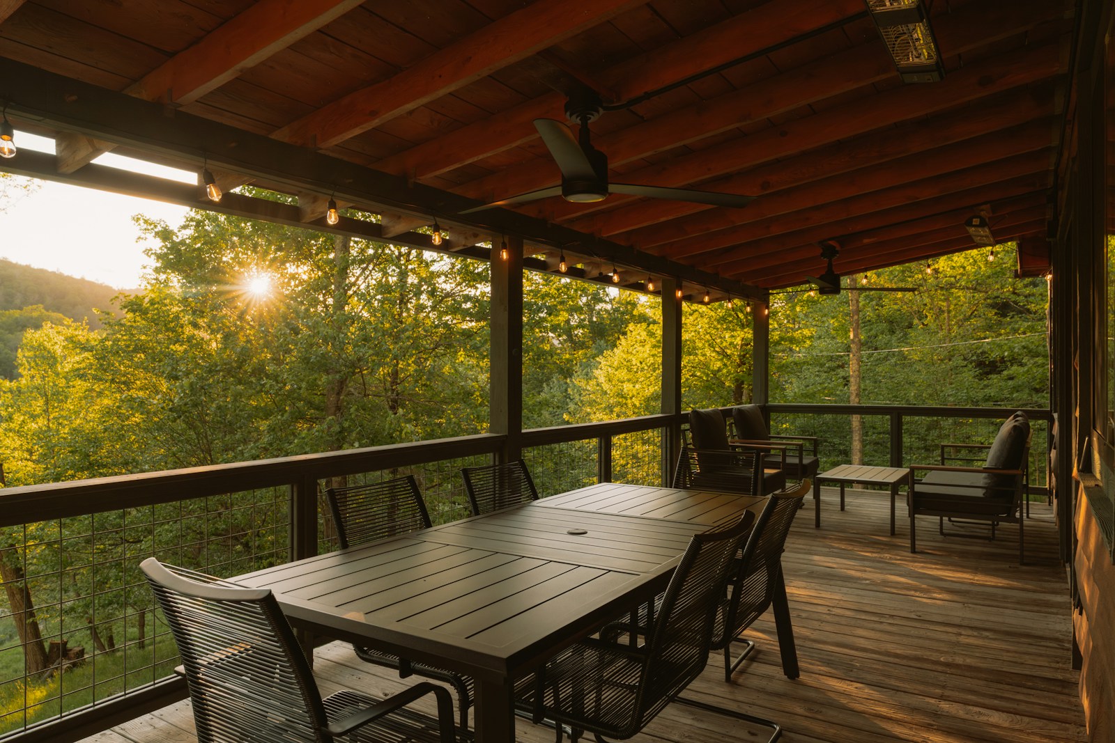 Guirlande à ampoules tendue au-dessus d'une table de repas sur une terrasse en bois.