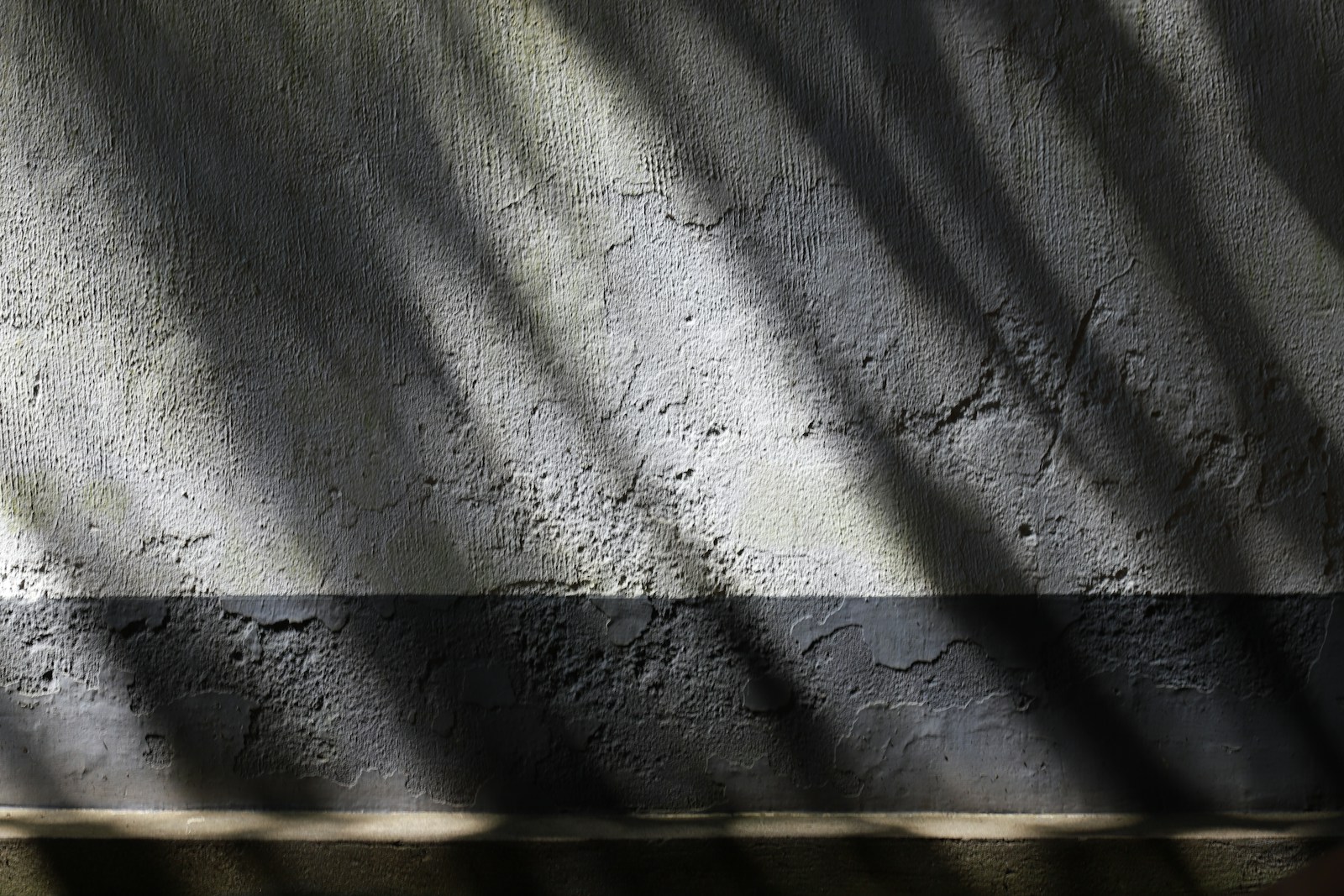 Lumière rasante dessinant des ombres sur un mur enduit blanc