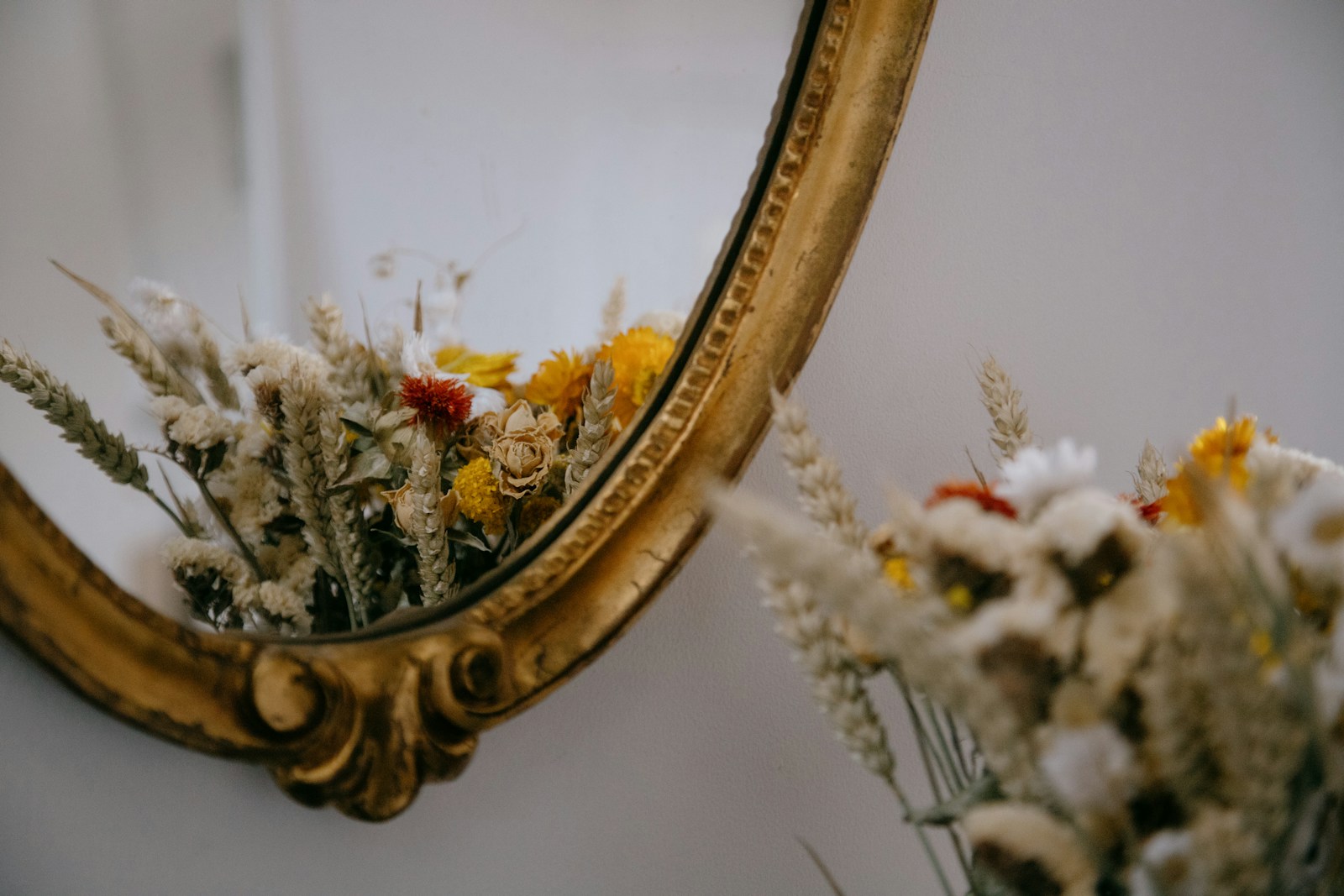 Miroir ancien doré, fleurs séchées et chandeliers posés sur une commode.