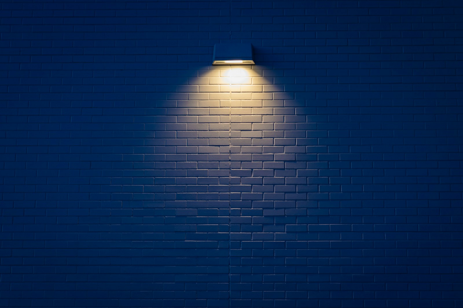 Mur bleu profond réchauffé par une applique en laiton et un miroir