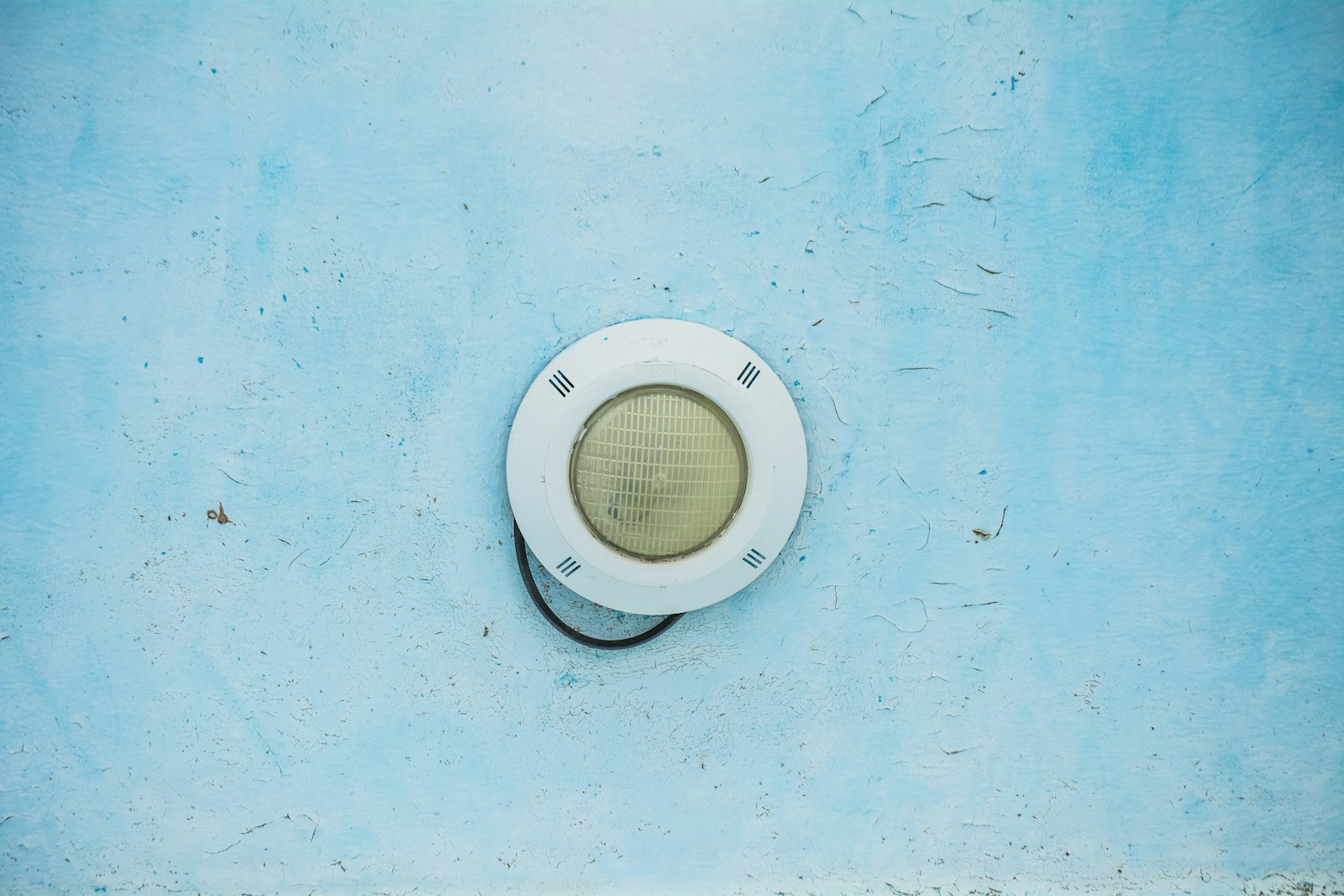 Projecteur à lumière blanche et froide allumé sur un mur extérieur en béton.