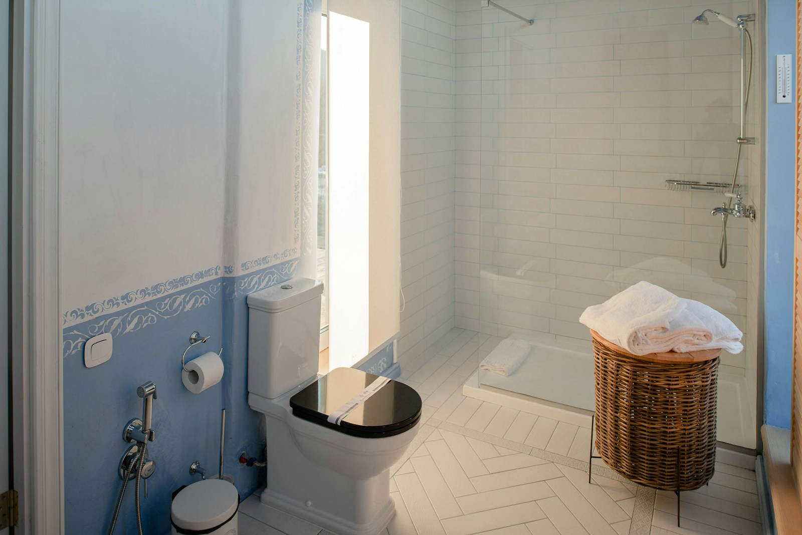 Salle de bain en carrelage blanc avec tabouret en bois et panier tressé.