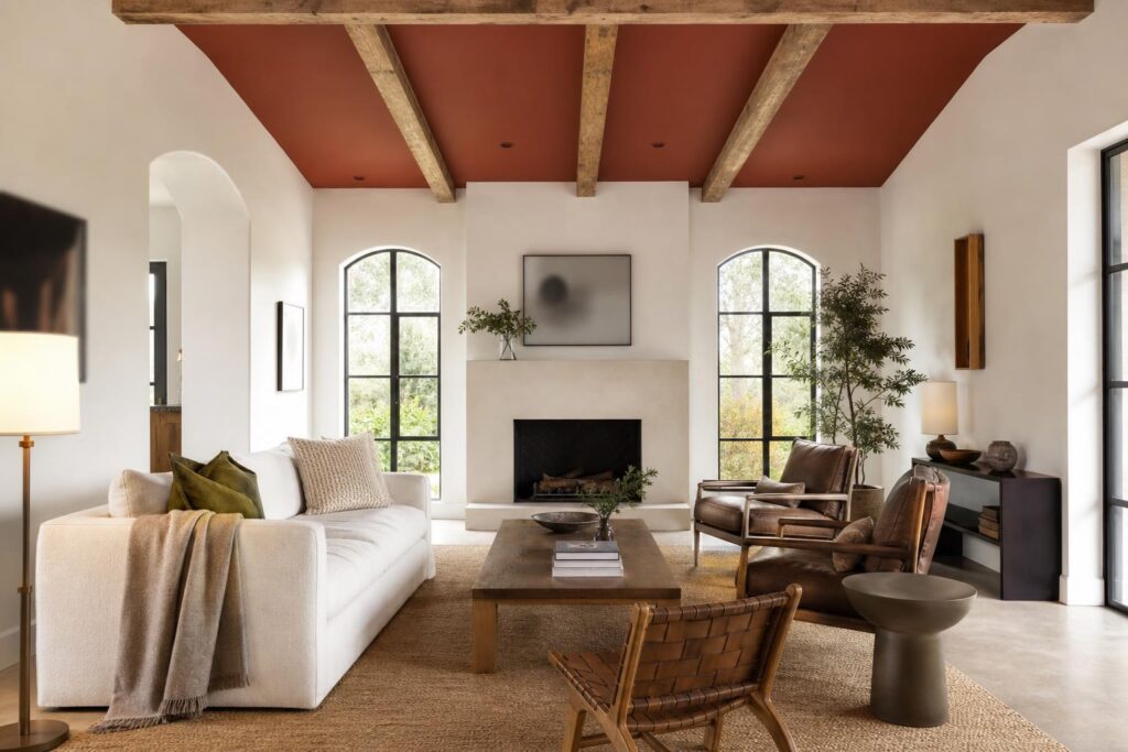 Salon aux murs clairs avec plafond peint en terracotta profond et poutres de bois apparentes.