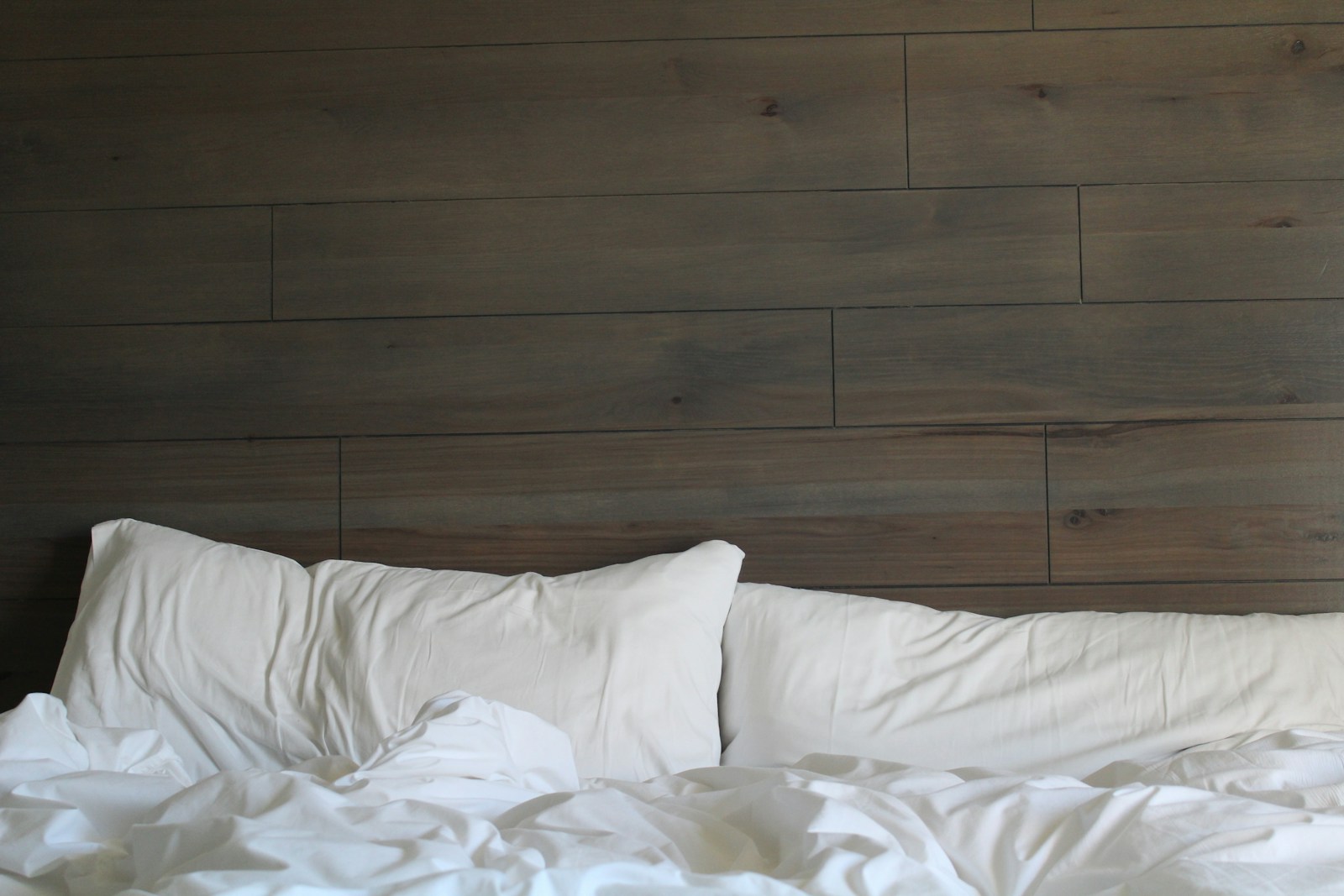 Tête de lit en tasseaux de bois dans une chambre aux tons naturels.