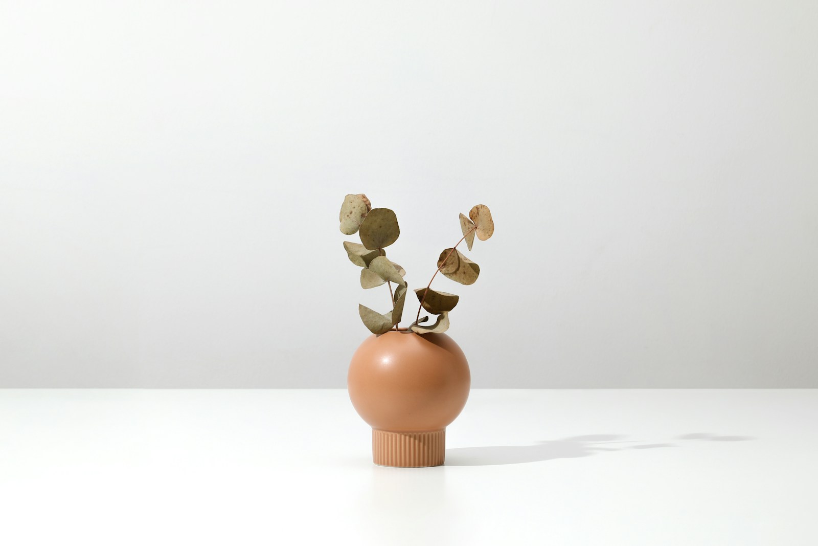 Vase en céramique couleur rouille sur une étagère en bois devant un mur bleu gris.